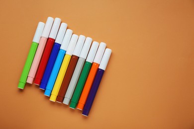 Photo of Different colorful markers on light brown background, flat lay. Space for text