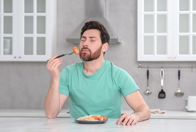 Photo of Man enjoying sausage and pasta at table in kitchen