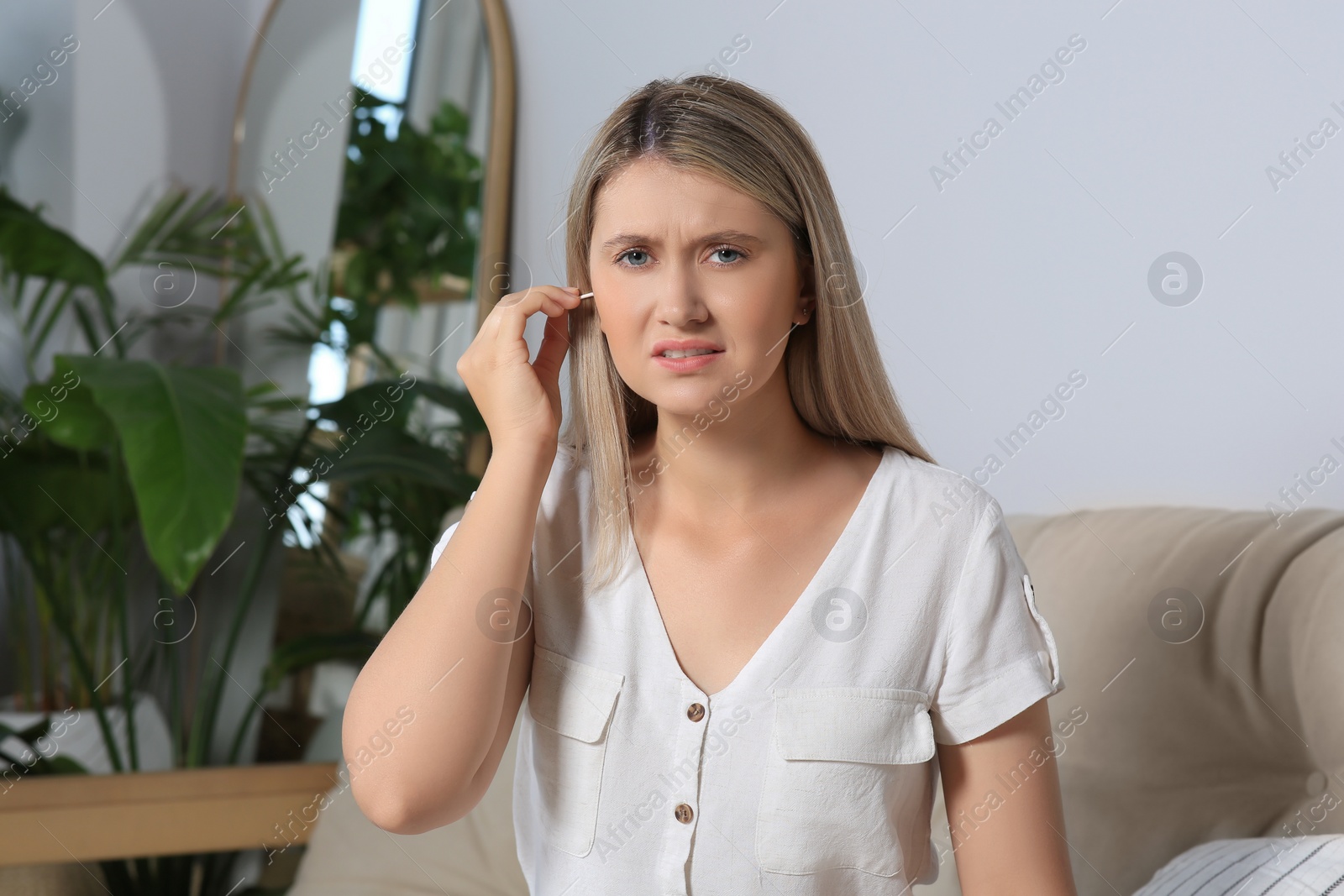 Photo of Young woman cleaning ear with cotton swab at home