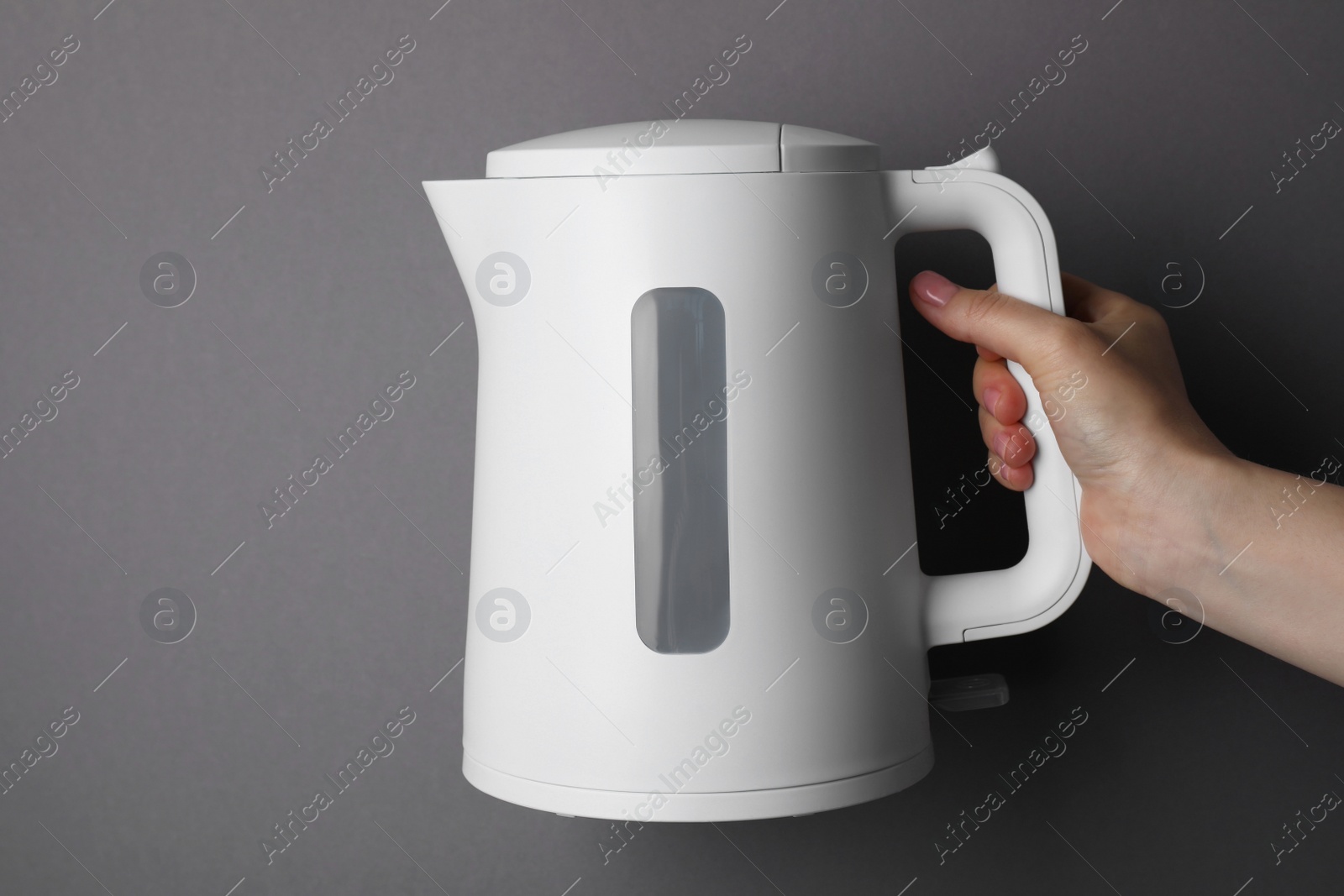 Photo of Woman holding modern electric kettle on grey background, closeup