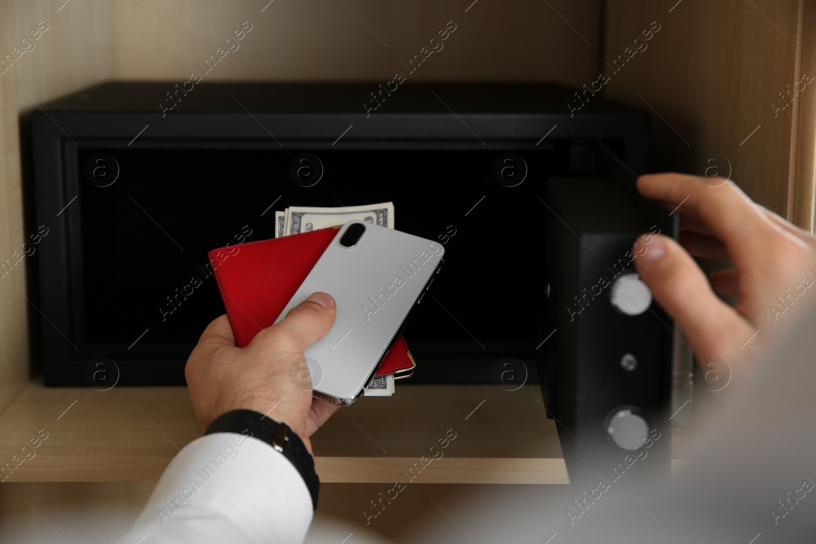Photo of Man putting smartphone, passport and money into steel safe, closeup