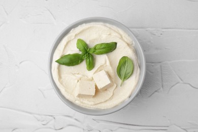 Photo of Delicious tofu sauce and basil leaves on white textured table, top view