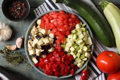 Cooking delicious ratatouille. Fresh ripe vegetables and plate on light blue wooden table, flat lay