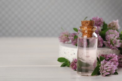 Beautiful clover flowers and bottle of essential oil on white wooden table. Space for text