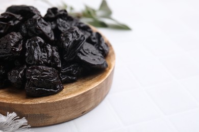 Photo of Sweet dried prunes on white tiled table, closeup. Space for text