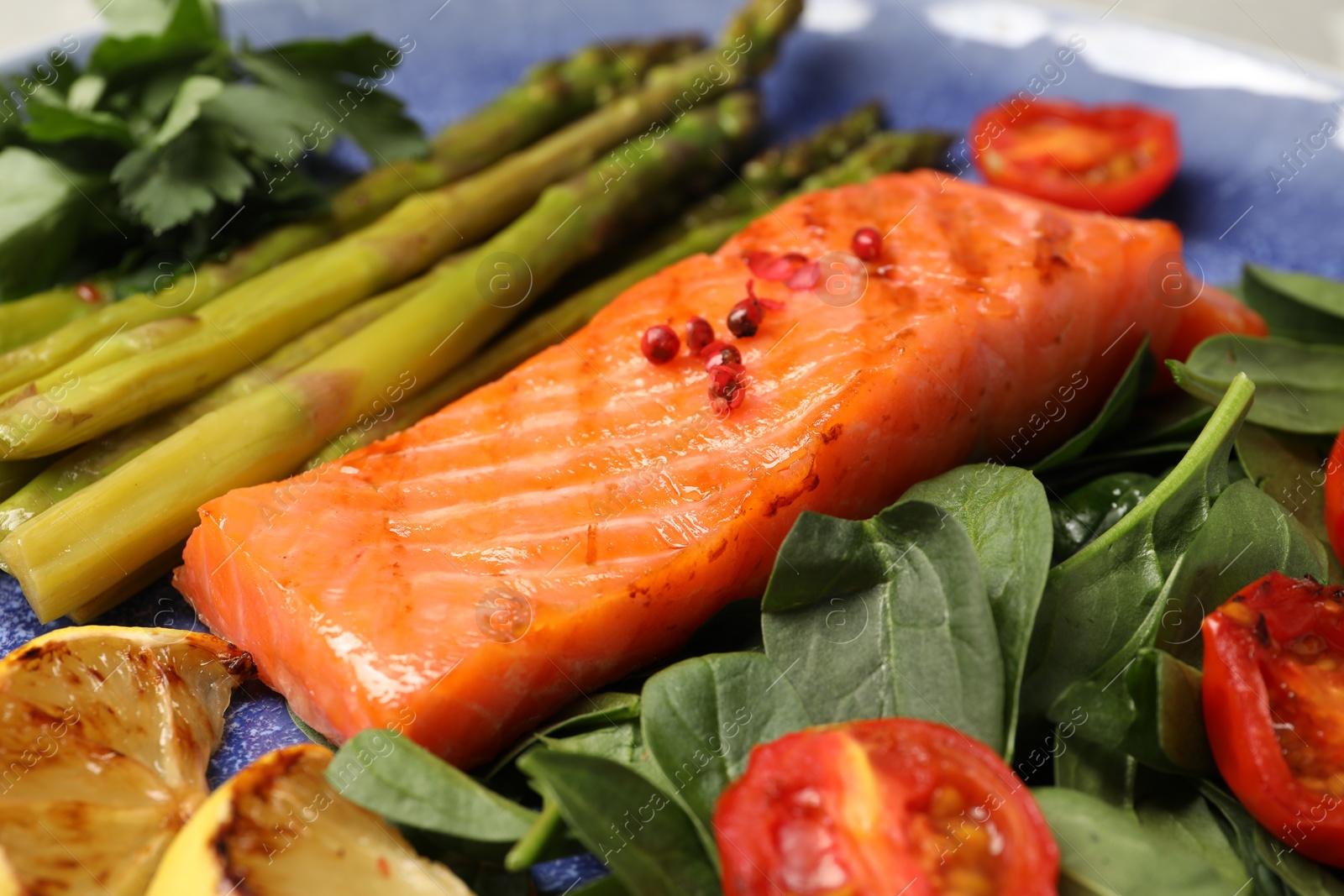 Photo of Tasty grilled salmon with tomatoes, asparagus, lemon and basil, closeup