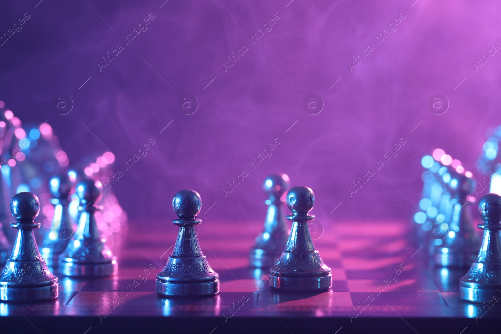 Photo of Chess pawns on checkerboard in color light, selective focus. Space for text