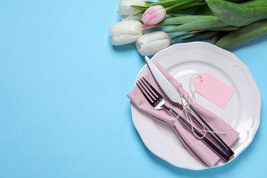 Photo of Stylish table setting with cutlery and tulips on light blue background, flat lay. Space for text