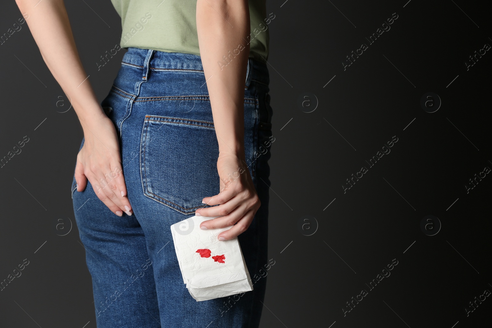 Photo of Woman holding toilet paper with blood stain on black background, space for text. Hemorrhoid concept