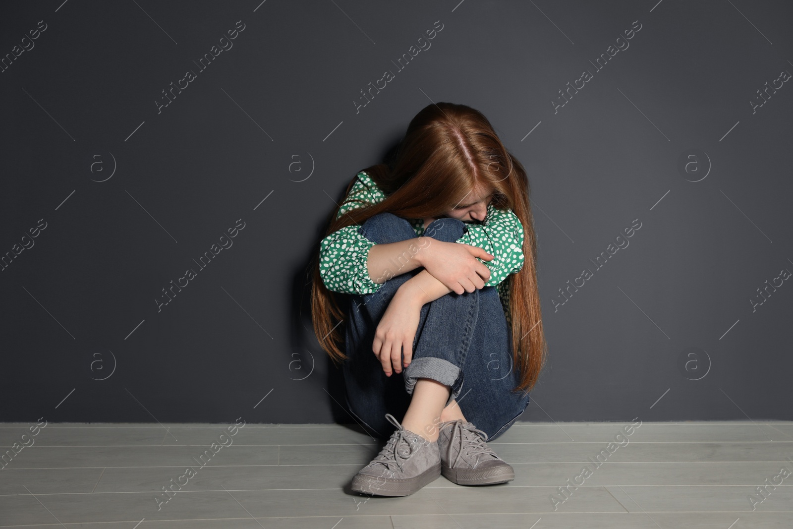 Photo of Upset young woman sitting on floor near grey wall