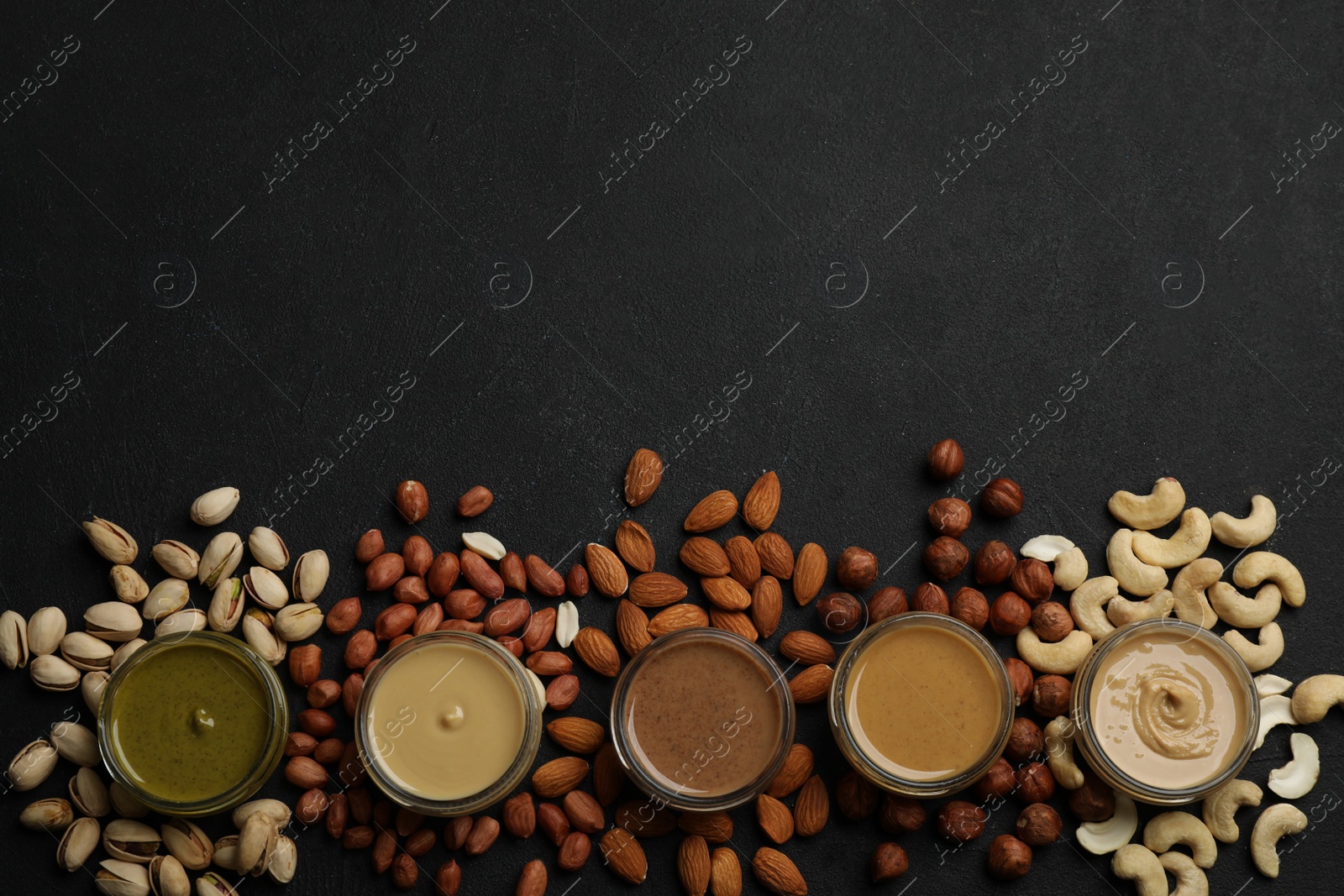 Photo of Jars with butters made of different nuts and ingredients on black table, flat lay. Space for text