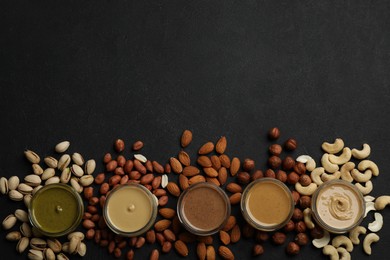 Jars with butters made of different nuts and ingredients on black table, flat lay. Space for text