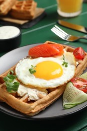 Photo of Delicious Belgian waffle with fried egg, salmon, cream cheese and vegetables served on green table, closeup
