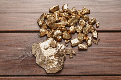 Photo of Pile of shiny gold nuggets on wooden table, flat lay