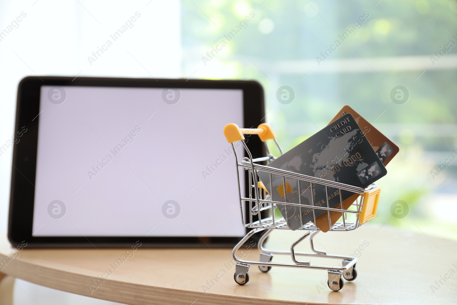 Photo of Internet shopping. Small cart with credit cards near modern tablet on table indoors