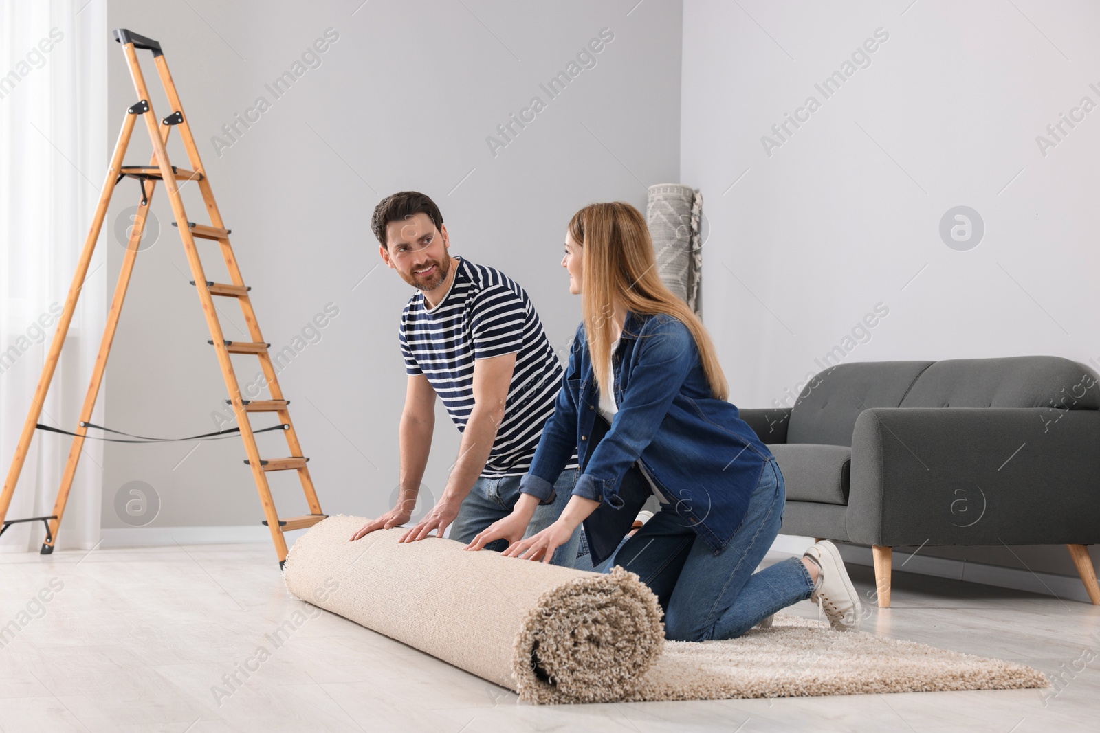 Photo of Smiling couple unrolling new carpet in room