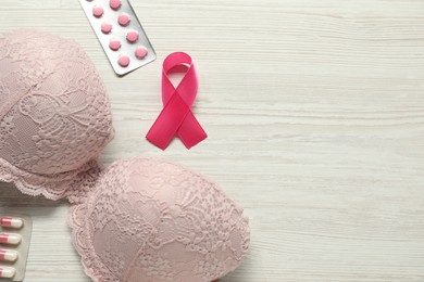 Photo of Breast cancer awareness. Pink ribbon, bra and pills on white wooden table, flat lay. Space for text