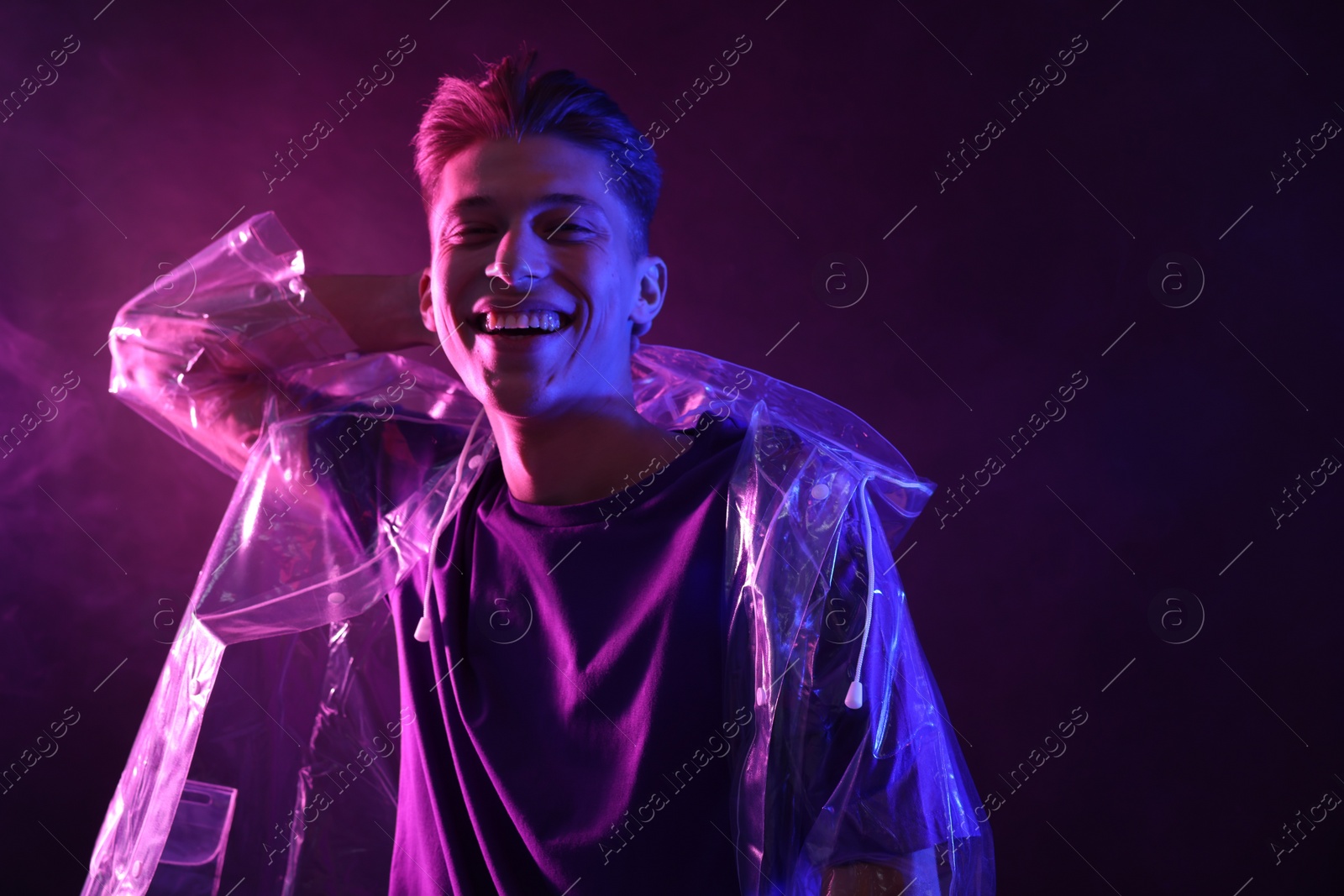 Photo of Young man wearing clear coat in neon lights with smoke effect. Space for text