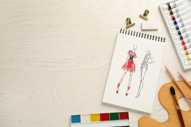 Sketches of different clothes in pad on white wooden table, space for text. Fashion designer's desk with stationery, flat lay