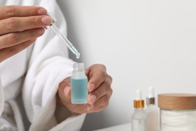 Woman with bottle of cosmetic serum at table, closeup. Space for text