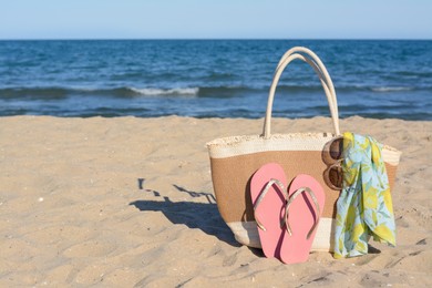 Photo of Straw bag with beach wrap, sunglasses and flip flops on sandy seashore, space for text. Summer accessories