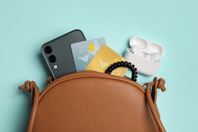 Photo of Stylish woman's bag with smartphone and accessories on light blue background, flat lay