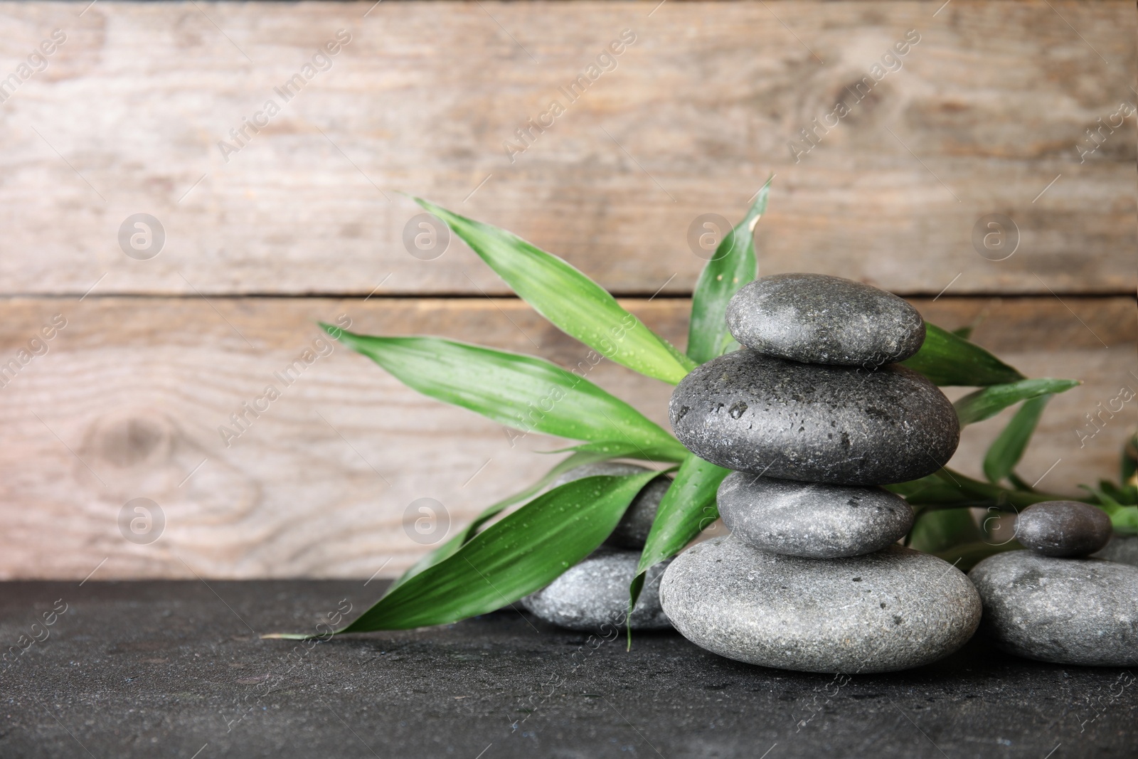 Photo of Stacked zen stones and bamboo leaves on table against wooden background. Space for text