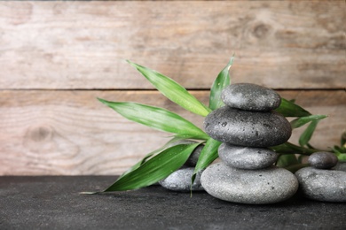 Photo of Stacked zen stones and bamboo leaves on table against wooden background. Space for text