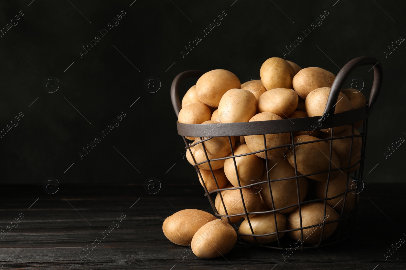 Photo of Raw fresh organic potatoes on wooden table against dark background. Space for text