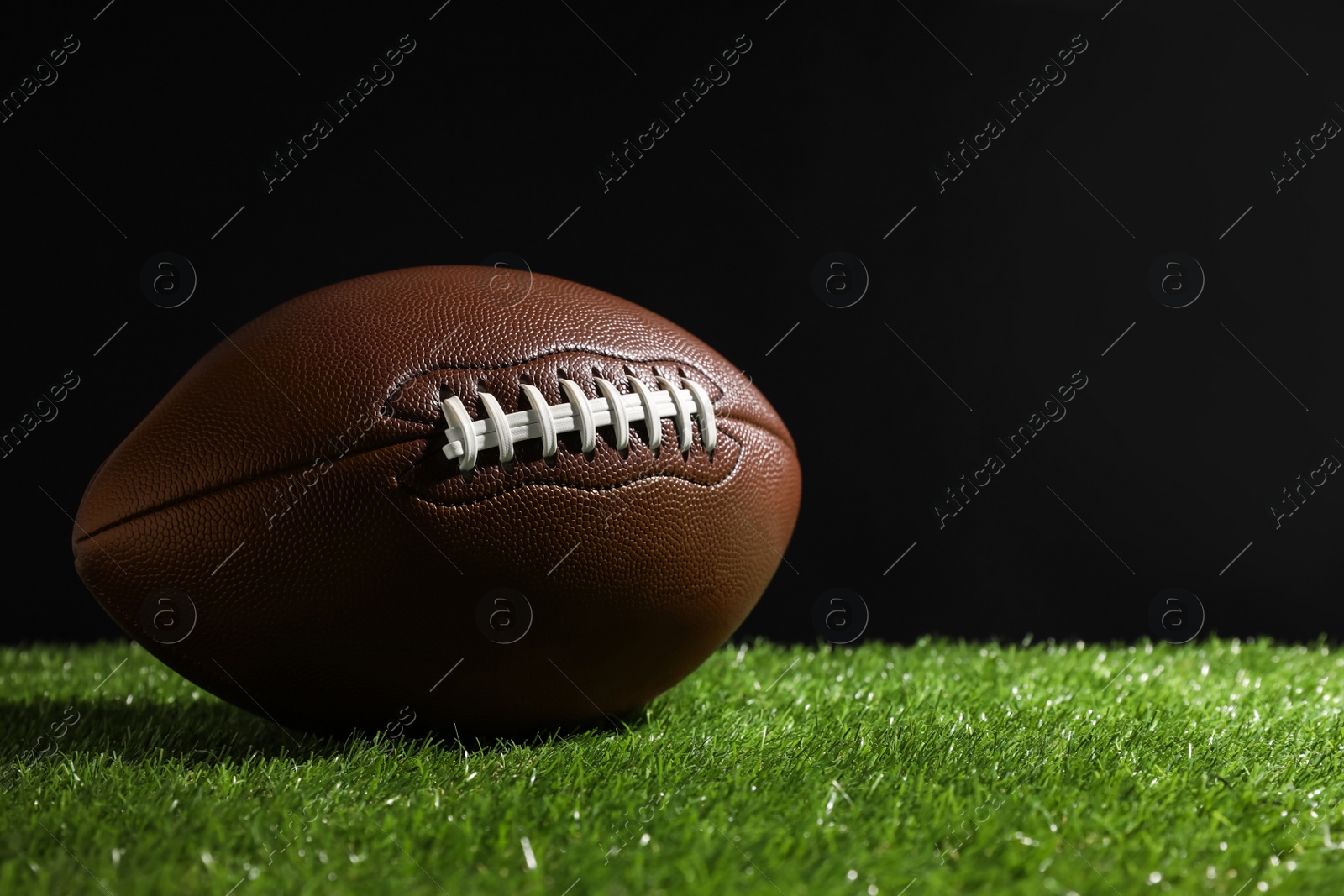 Photo of American football ball on green grass against black background. Space for text