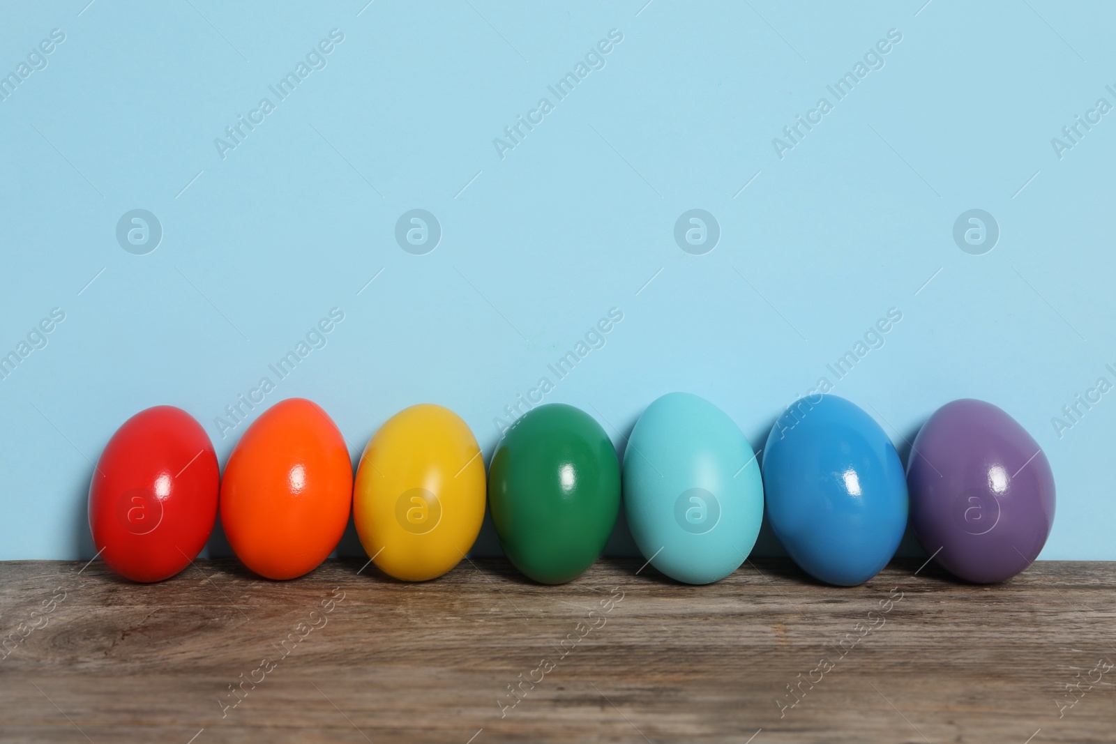 Photo of Easter eggs on wooden table against light blue background, space for text