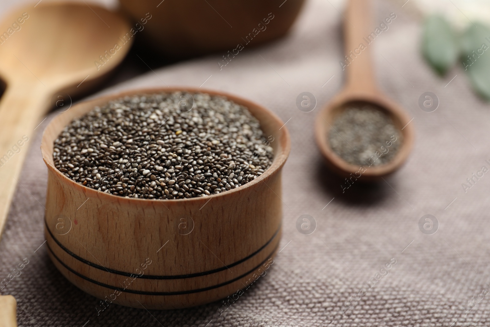 Photo of Chia seeds in wooden bowl on grey fabric, closeup. Space for text