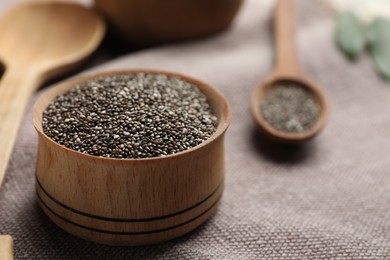 Photo of Chia seeds in wooden bowl on grey fabric, closeup. Space for text