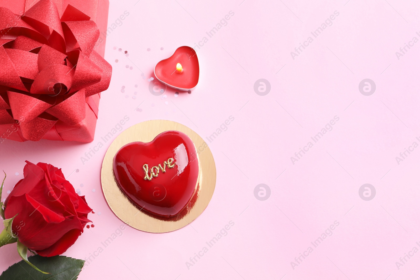 Photo of St. Valentine's Day. Delicious heart shaped cake, gift and rose on light pink background, flat lay. Space for text