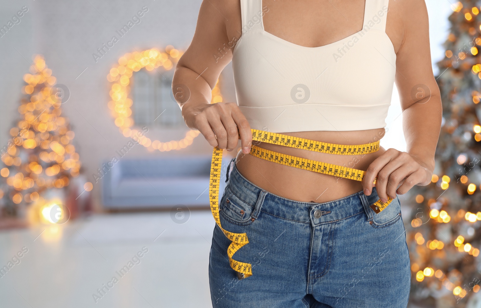 Image of Woman measuring waist with tape in room decorated for Christmas, closeup