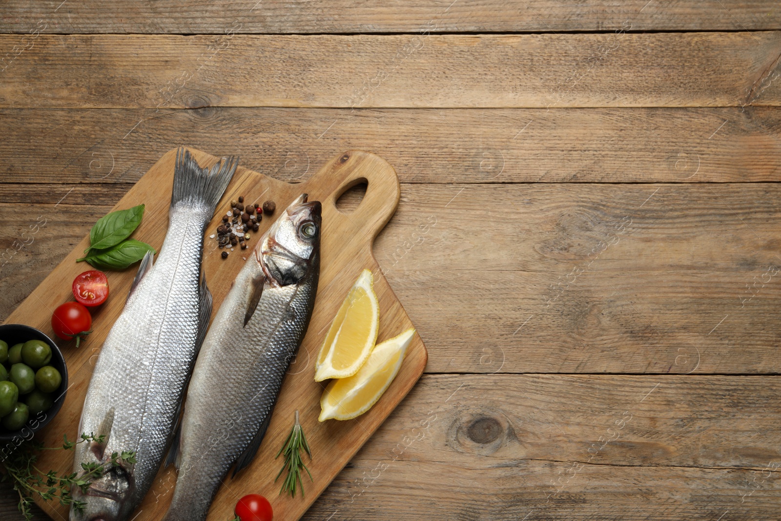 Photo of Sea bass fish and ingredients on wooden table, top view. Space for text