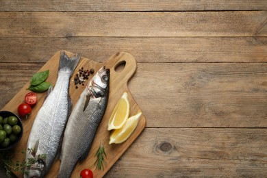 Photo of Sea bass fish and ingredients on wooden table, top view. Space for text