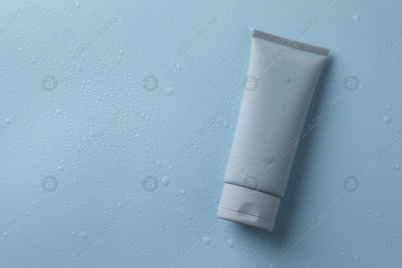 Photo of Moisturizing cream in tube on light blue background with water drops, top view. Space for text