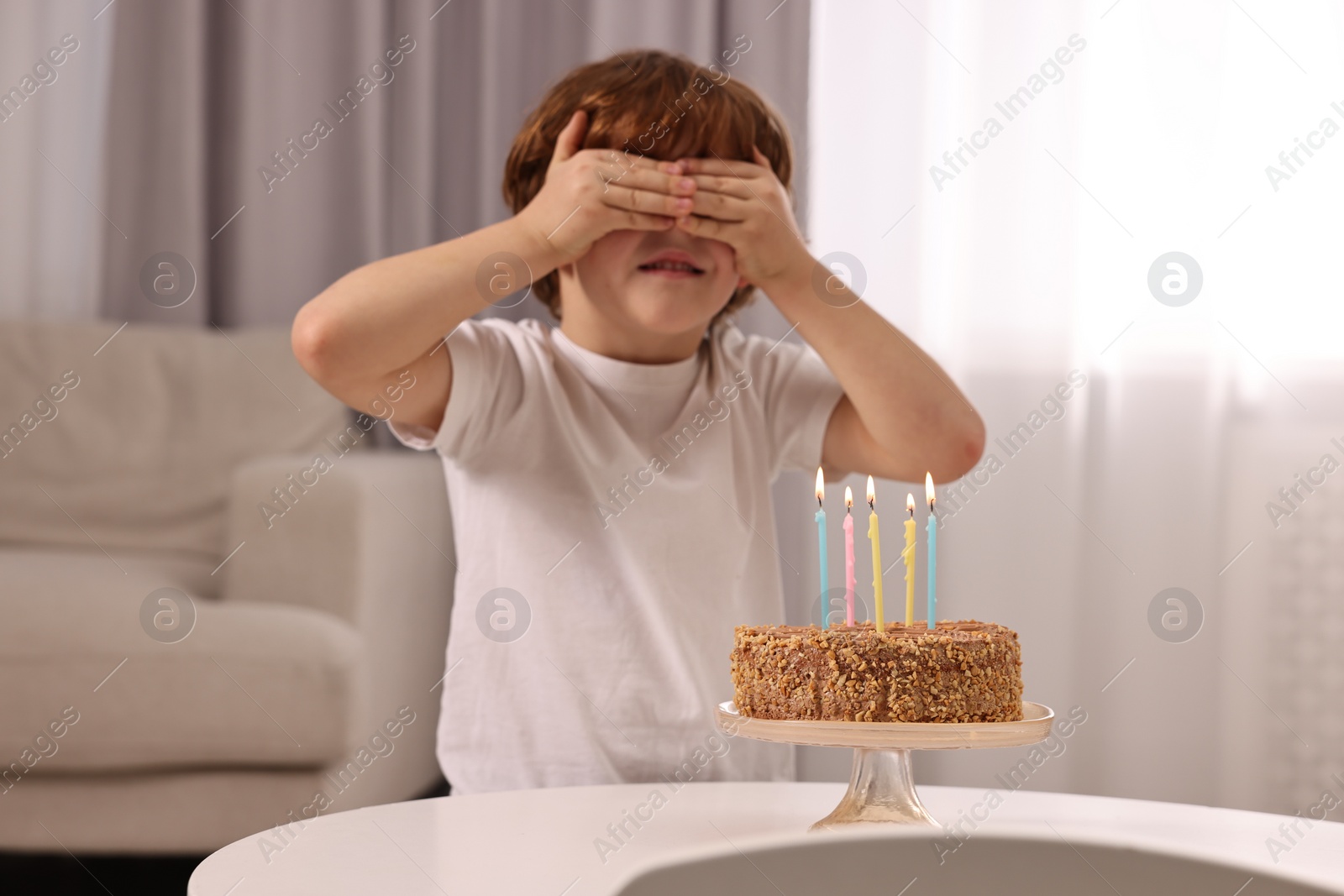 Photo of Cute boy with birthday cake at table indoors