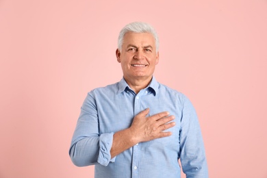 Photo of Portrait of mature holding hand on his heart against color background