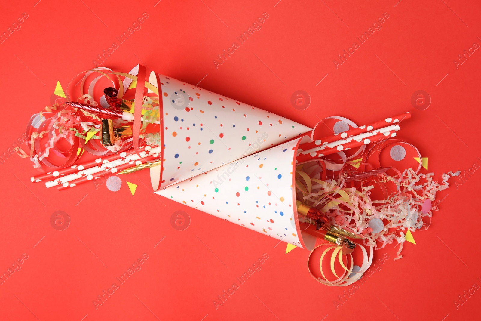 Photo of Party hats and different festive items on red background, flat lay