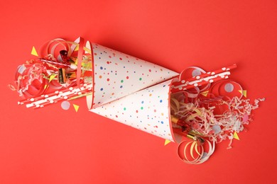 Photo of Party hats and different festive items on red background, flat lay