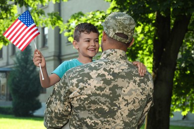 Soldier and his little son with American flag outdoors. Veterans Day in USA
