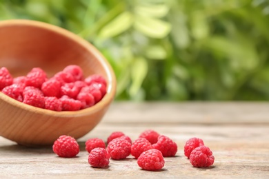 Bowl with ripe aromatic raspberries on table against blurred background