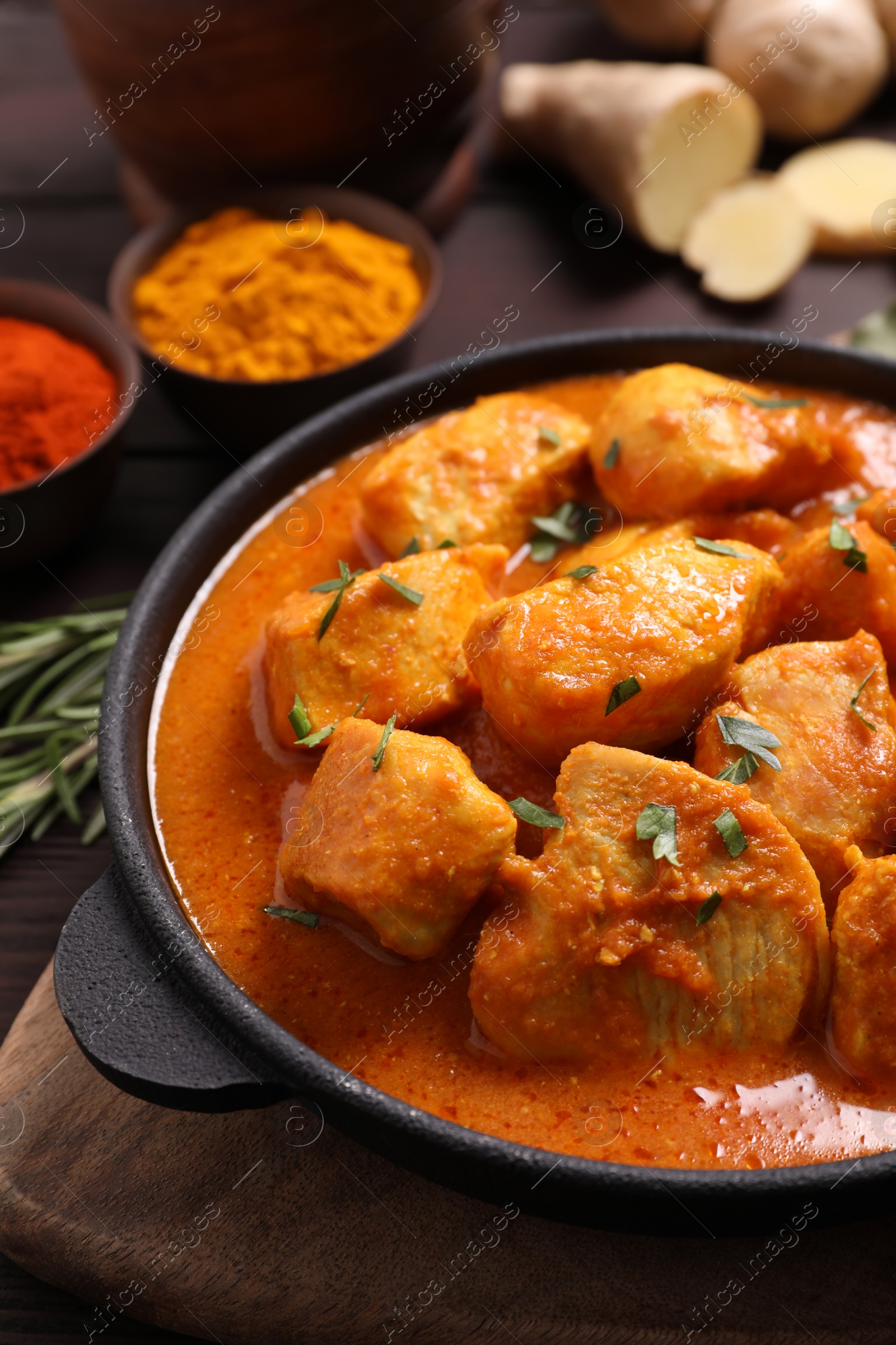 Photo of Delicious chicken curry in pan on wooden board, closeup