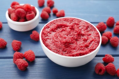 Photo of Raspberry puree in bowl and fresh berries on blue wooden table, closeup