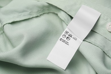 Clothing label with care recommendations on light green garment, top view. Space for text