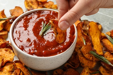 Photo of Woman dipping sweet potato chip in red sauce at table, closeup