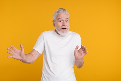 Portrait of surprised senior man on yellow background