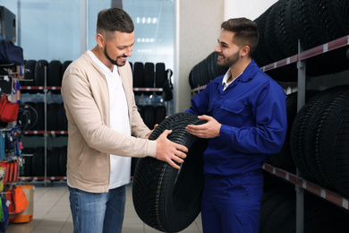 Photo of Mechanic helping client to choose car tire in auto store